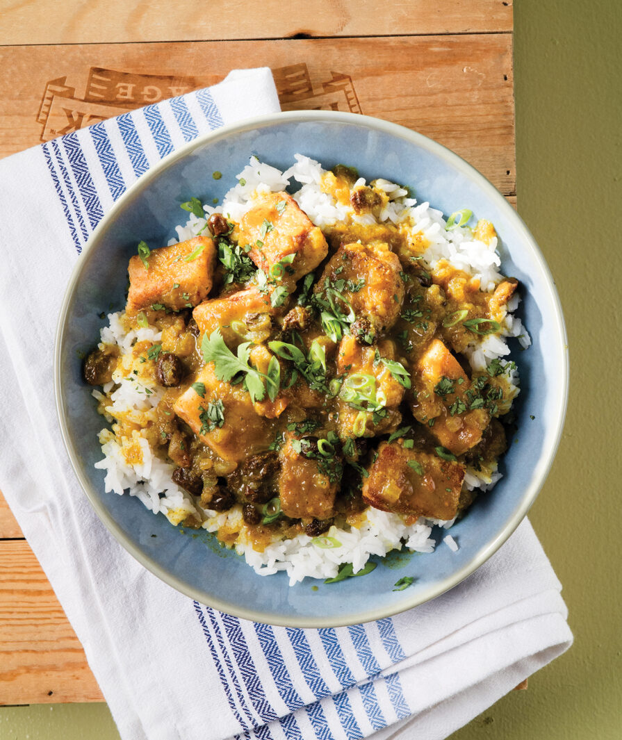 Curried Fish served in a blue plate with a blue and white napkin sitting underneath it on top of a wood and green painted surface.